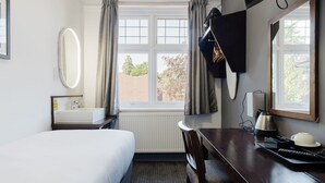 Une chambre d’hôtel avec un lit, un bureau avec une lampe, un miroir et une fenêtre avec des rideaux.