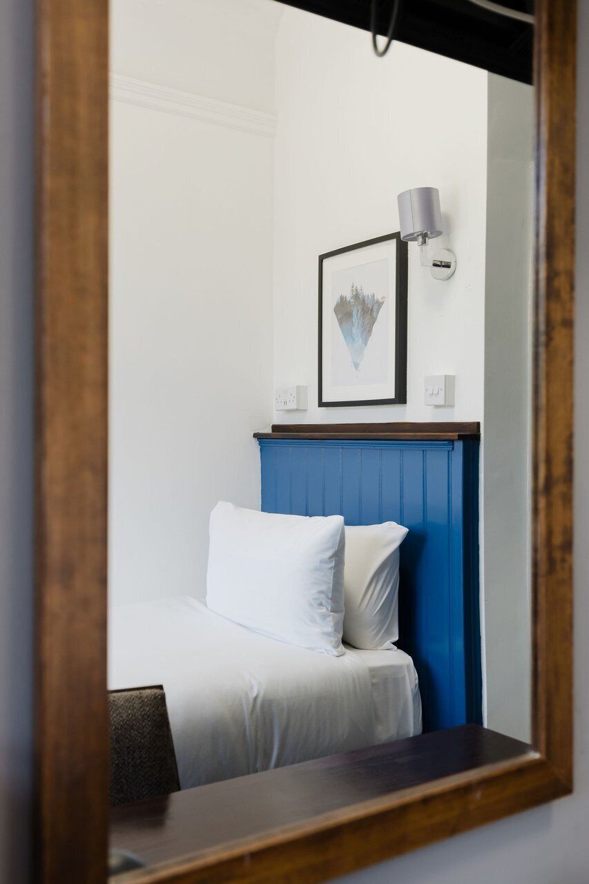 A bedroom with a bed, a blue headboard, a framed picture, and a wall-mounted lamp.