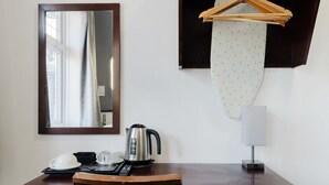 A hotel room with a wooden desk, a kettle, a remote control, a mirror, a hanging garment, and a white lamp. - Single Room Clean & Practical Stay in Watford (Watford)