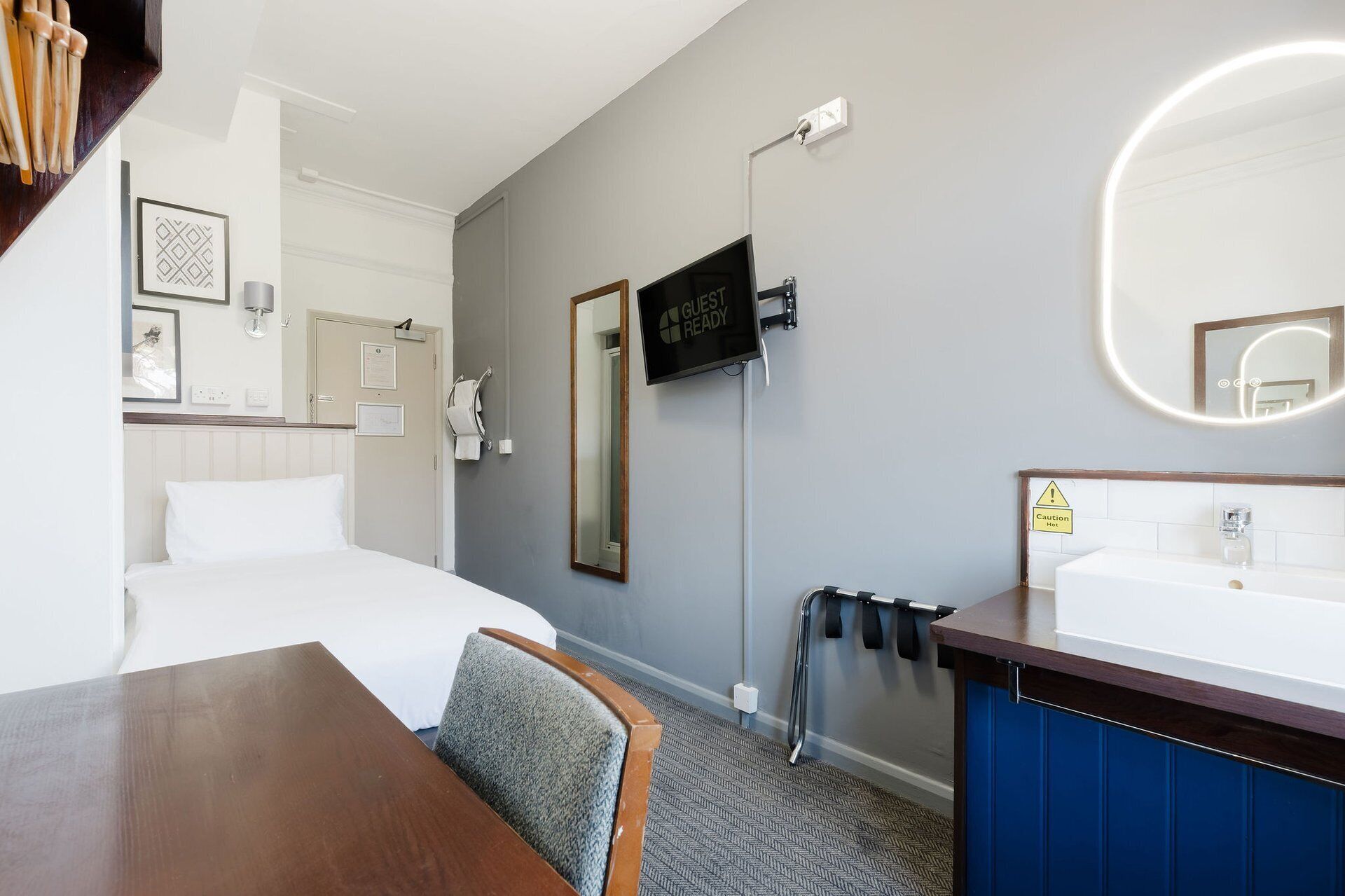 Een hotelkamer met een bed, een bureau, een televisie, een spiegel, een wastafel en een handdoekrek.