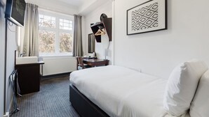 A hotel room with a bed, a desk with a chair, a TV, a radiator, and a window with curtains. - Single Room Clean & Practical Stay in Watford (Watford)