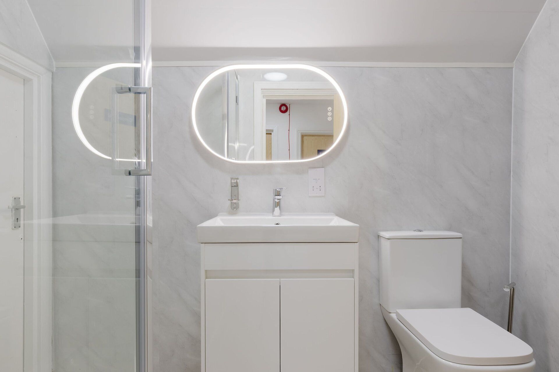 A modern bathroom with a glass shower enclosure, a white sink, a toilet, and a mirror with integrated lighting.