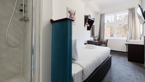 Ein Hotelzimmer mit einem Bett, einem Schreibtisch, einem Sessel, einem Fenster mit Vorhängen, einer Dusche und einem Bild an der Wand.
