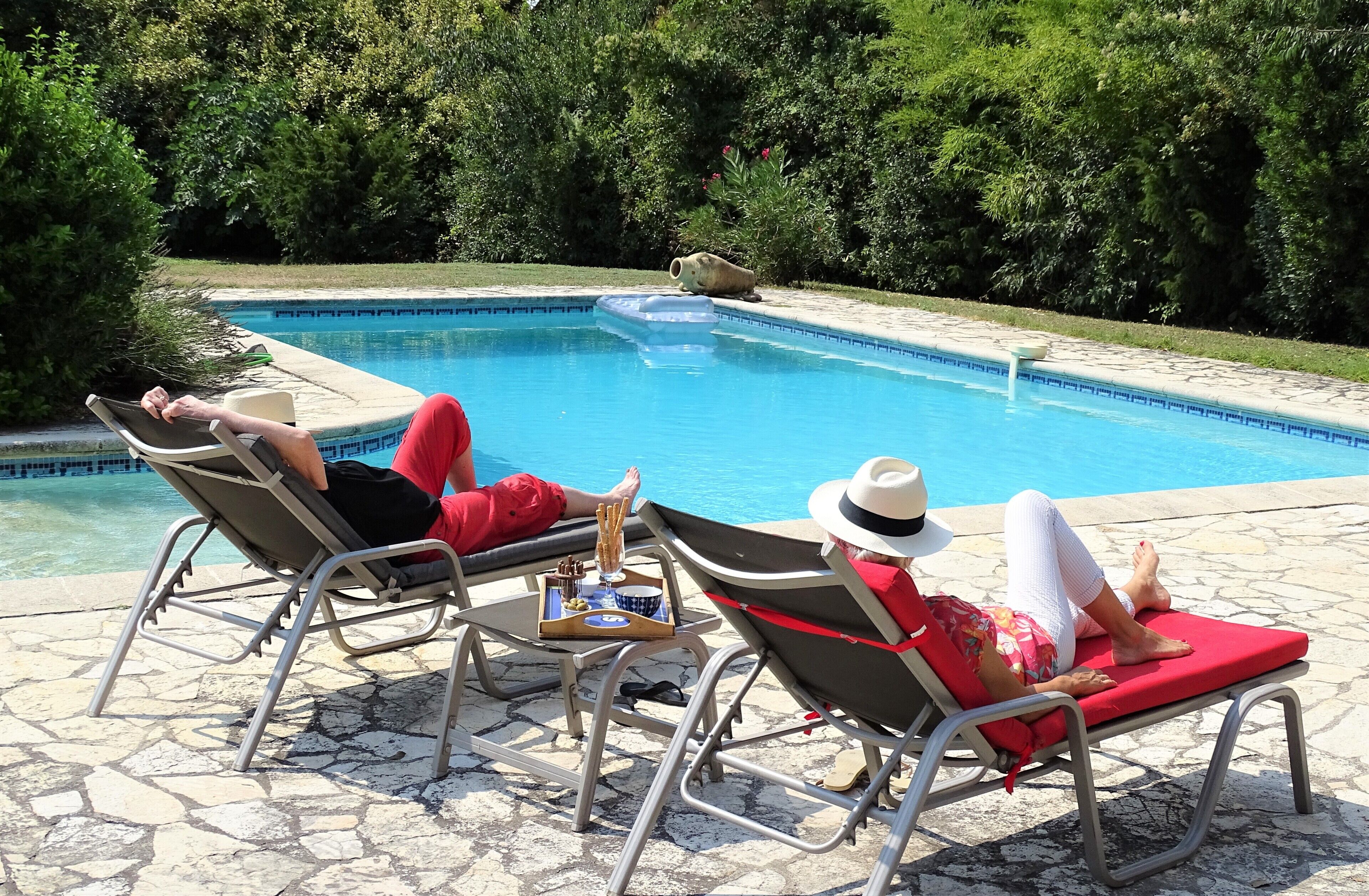 Uma área ao lado da piscina com espreguiçadeiras, piscina e um pátio de pedra.