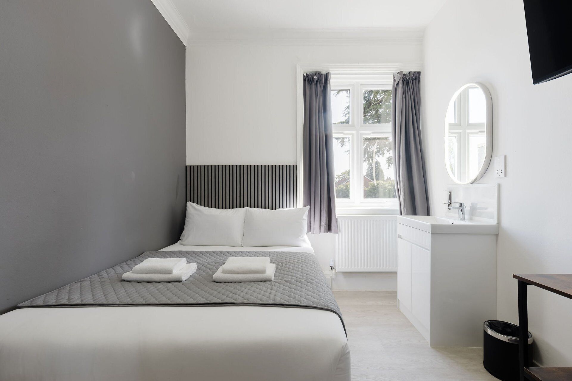 Un dormitorio moderno con cama, mesita de noche y ventana con cortinas.