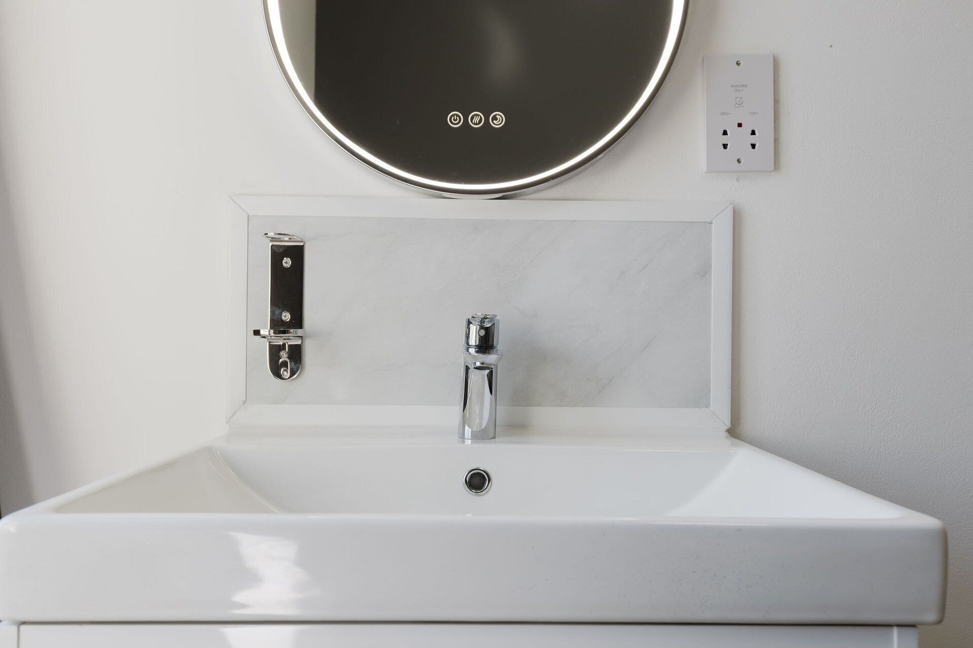 A bathroom with a white sink, a mirror, and a wall-mounted light switch.