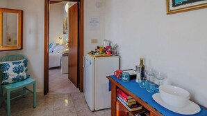 A small kitchenette with a refrigerator, a table with a blue tablecloth, and a chair with a blue cushion.