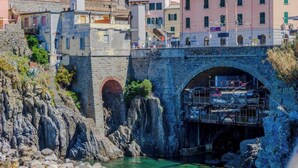 A stone bridge with an arch, a rocky shoreline, and buildings in the background.