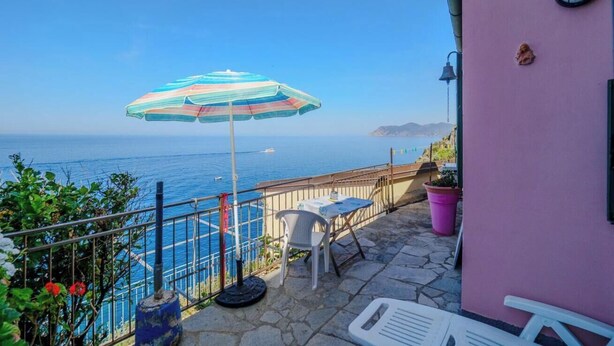 A balcony with a view of the sea, a striped umbrella, and a table with a chair.