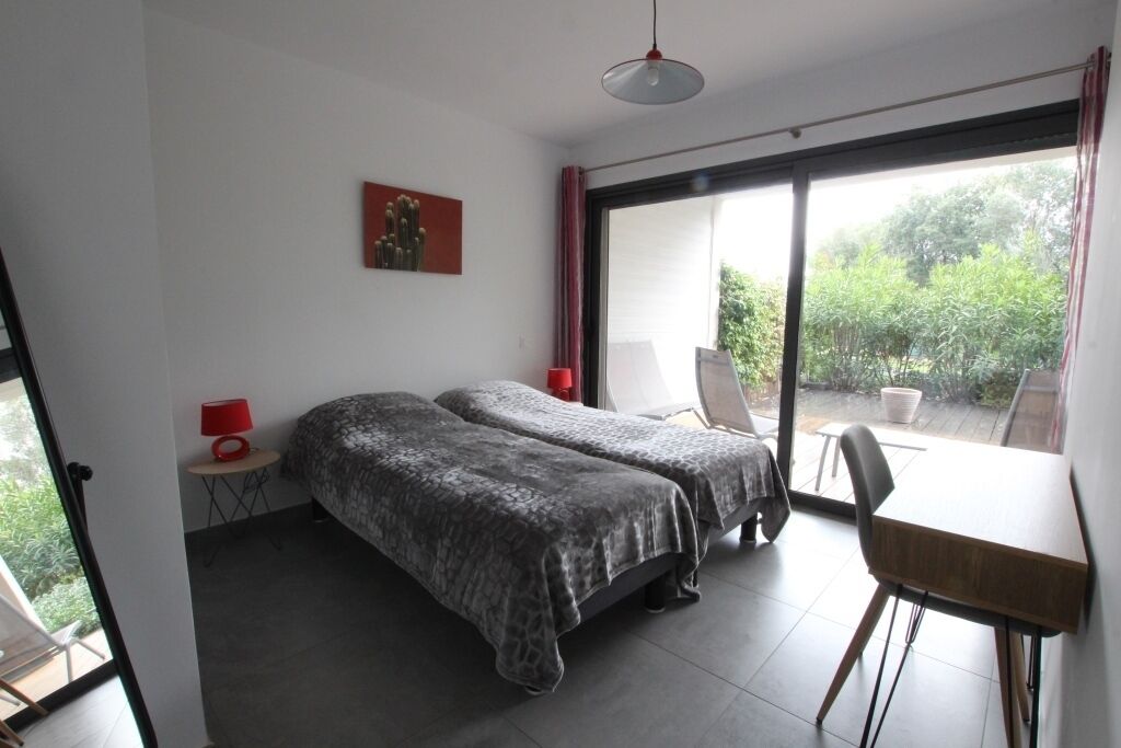 A bedroom with two beds, a desk, a chair, a red lamp, and a cactus painting.