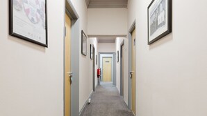 A hallway with framed pictures on the walls, a fire extinguisher, and a door labeled 'EXIT' at the end. - Comfortable King room with Private Bathroom (Watford)