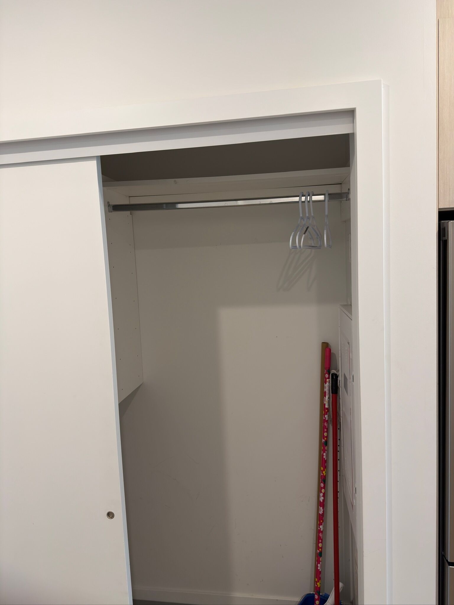 A white closet with a hanging rod and a broom leaning against the wall.