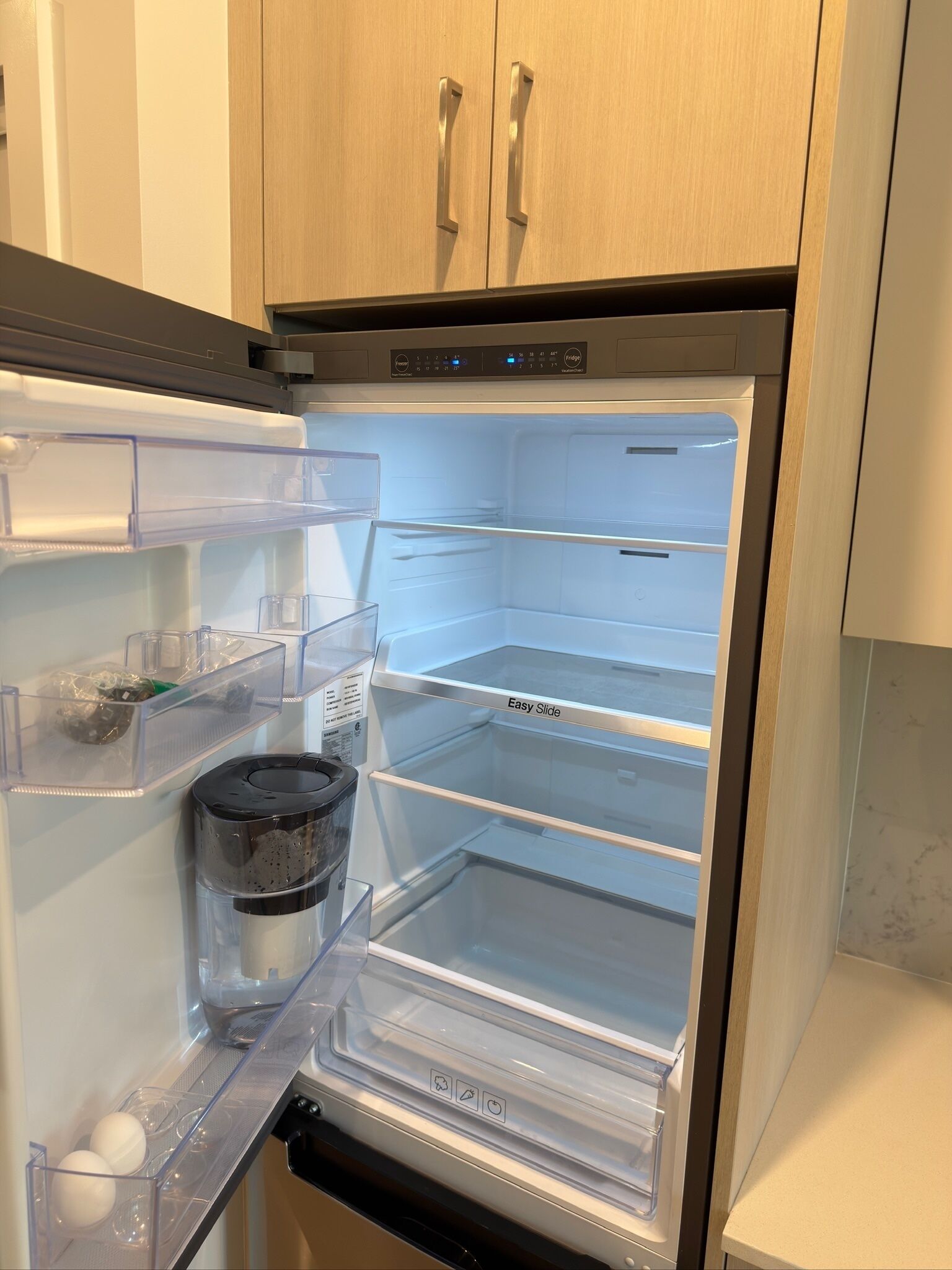 A stainless steel refrigerator with a freezer compartment, a water dispenser, and a transparent door.