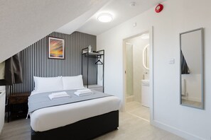 A modern bedroom with a bed, bedside table, and a painting on the wall. - Comfortable King Room with Private Bathroom (Watford)