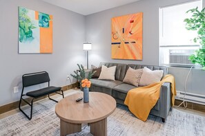 A modern living room with a sofa, a coffee table, and a chair. There are two abstract paintings on the walls. - Lancaster Art Suite 2 | 4BR near Drexel & Penn (Philadelphia)