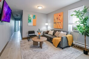 A modern living room with a sofa, coffee table, and artwork on the walls. - Lancaster Art Suite 2 | 4BR near Drexel & Penn (Philadelphia)