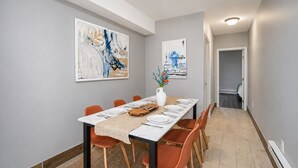 A dining area with a long table set for six, orange chairs, a white vase with flowers, and abstract art on the walls. - Lancaster Art Suite 2 - 4BR near Drexel & Penn (Philadelphia)