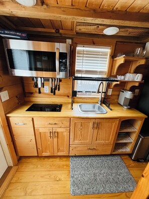 Una cocina compacta con gabinetes de madera, un lavamanos de acero inoxidable, un microondas y una ventana con persianas.