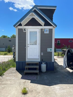 A small, single-story building with a white door, a small porch, and a gas cylinder outside. - Cozy 1-bedroom cabin in terrific Newport with AC (Newport)