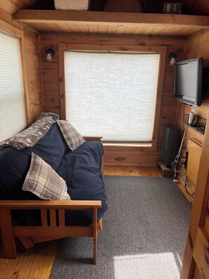 A wooden cabin room with a bed, a window, a television, and a heater. - Cozy 1-bedroom cabin in terrific Newport with AC (Newport)