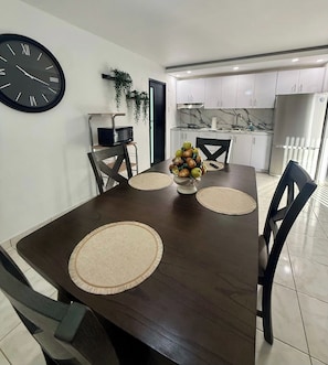 A dining area with a dark wooden table, a clock on the wall, and a kitchen in the background. - Central House w/Free Parking, Near Beach & (Carolina)