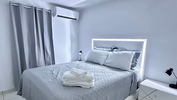 Ein modernes Schlafzimmer mit Bett, Nachttisch, Klimaanlage und einem Fenster mit Vorhängen.