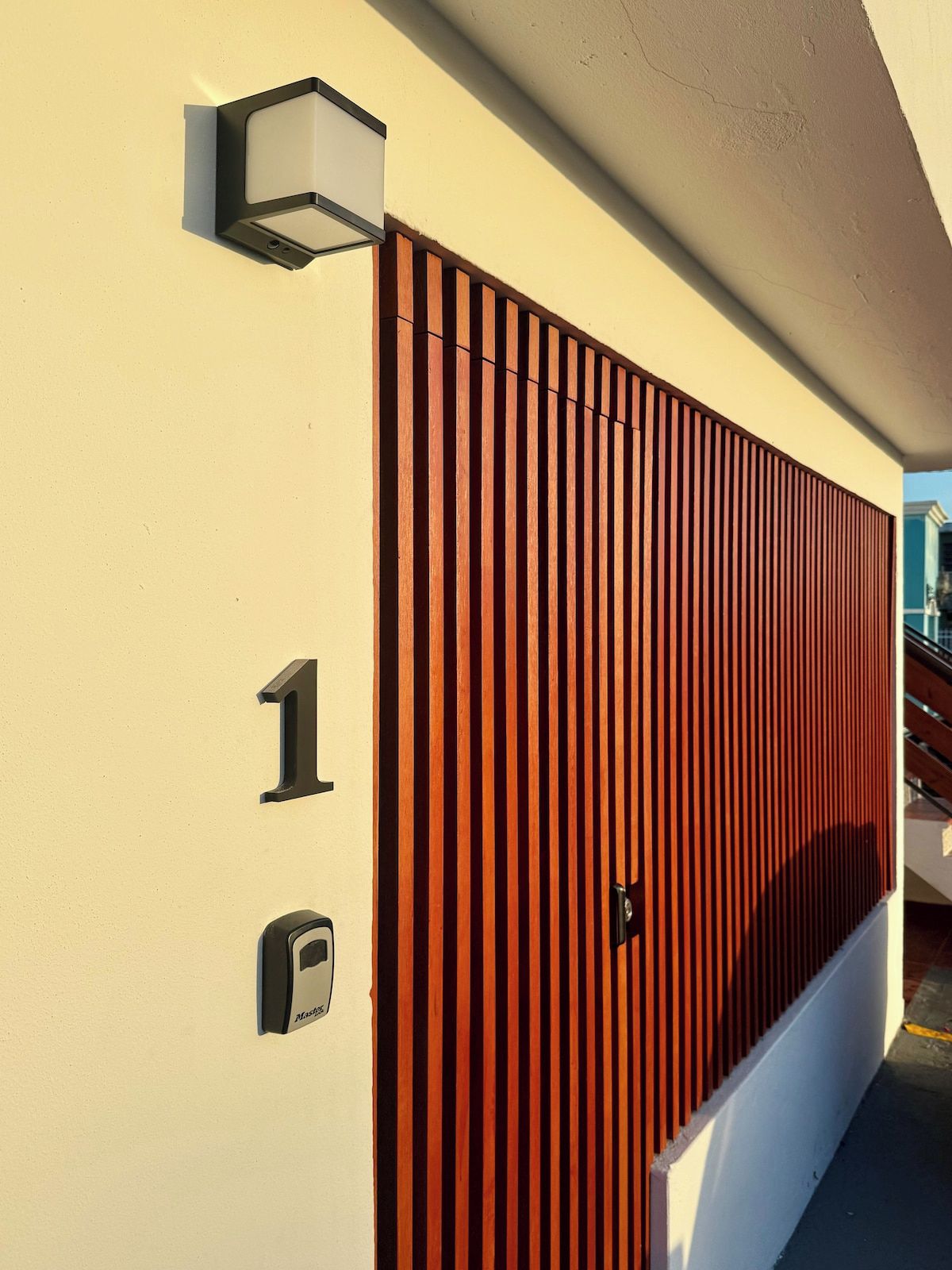 Facciata moderna di un edificio caratterizzata da pannelli verticali in legno, una cassetta postale e il numero '16'.