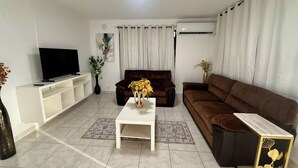 Ein Wohnzimmer mit Fernseher, einem braunen Sofa, einem weißen Couchtisch und einem kleinen Beistelltisch mit einer Vase.