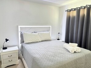 A neatly made bed with a white headboard, a bedside table with a lamp, and a set of towels. - Central House w/Free Parking, Near Beach & (Carolina)