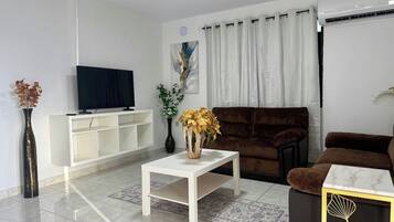 Una sala de estar moderna con un televisor de pantalla plana, una consola blanca, un sofá marrón y un jarrón decorativo con flores amarillas.