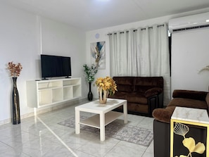 A modern living room with a flat-screen TV, a white console table, a brown sofa, and a decorative vase with yellow flowers. - Central House w/Free Parking, Near Beach & (Carolina)