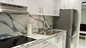 Eine moderne Küche mit weißen Schränken, einer schwarzen Marmor-Spritzschutzleiste, Edelstahlgeräten und einem gemusterten Teppich.