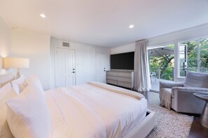 A bedroom with a large bed, a TV, a dresser, and a balcony with a view of greenery. - Miller Heights - Sunset Strip, unobstructed city and jetliner views (Los Angeles)
