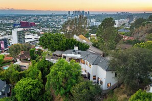 A residential area with a large house featuring a balcony, surrounded by lush greenery and a city skyline in the background. - Miller Heights - Sunset Strip, unobstructed city and jetliner views (Los Angeles)