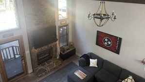 Un salon avec une cheminée en pierre, un lustre, un canapé et un drapeau accroché au mur.