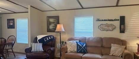 Uma sala de estar com um sofá de couro marrom, uma poltrona marrom, um ventilador de teto e uma parede com uma placa de boas-vindas.