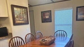 Un comedor con una mesa y sillas de madera, un ventilador de techo y cuadros en las paredes.