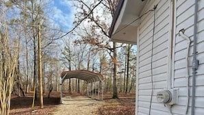 A gravel driveway leading to a covered outdoor area with a metal structure, a house with white siding, and utility lines on the side. - Reel'em Inn fishing cabin in the Heart of Pickwick (Hardin County)