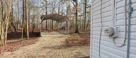 A gravel driveway leading to a covered outdoor area with a metal structure, a house with white siding, and utility lines on the side.