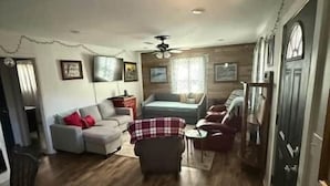 A spacious living room with a sofa, armchairs, and a coffee table. There is a ceiling fan and a door with a window. - Reel'em Inn fishing cabin in the Heart of Pickwick (Hardin County)