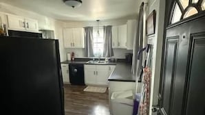 A kitchen with white cabinets, a black refrigerator, and a window with curtains. - Reel'em Inn fishing cabin in the Heart of Pickwick (Hardin County)