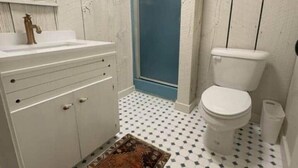 A bathroom with a white sink, a toilet, and a shower. - The Bungalow at Bear Creek (Tishomingo County)