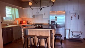 A kitchen with a central island, bar stools, a refrigerator, and a window. - The Bungalow at Bear Creek (Tishomingo County)