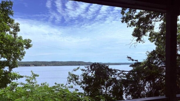 A view from a covered deck overlooking a body of water with trees in the foreground. - The Bungalow at Bear Creek (Tishomingo County)