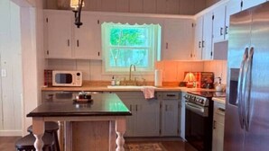 A kitchen with wooden cabinets, a central island with stools, a microwave, a stove, and a refrigerator. - The Bungalow at Bear Creek (Tishomingo County)