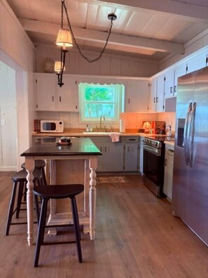 Une cuisine avec des meubles en bois, un îlot central doté de tabourets, un four à micro-ondes, une cuisinière et un réfrigérateur.