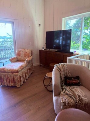 A living room with a television, a chair, a sofa, and a window.