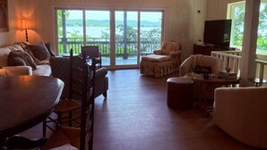 A spacious living room with a large sliding glass door leading to a balcony, a dining table, and a television. - The Bungalow at Bear Creek (Tishomingo County)