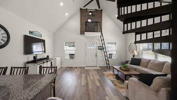En rummelig, loft-agtig opholdsstue med et køkken, spiseplads og et soveværelse i loftet med balkon.