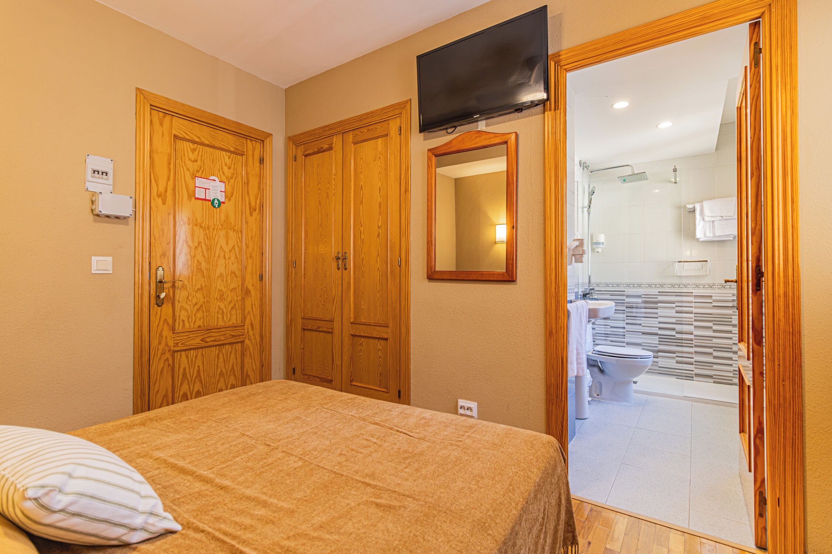 Habitación de hotel con cama, puertas de madera, un espejo y un baño visible a través de un acceso abierto.